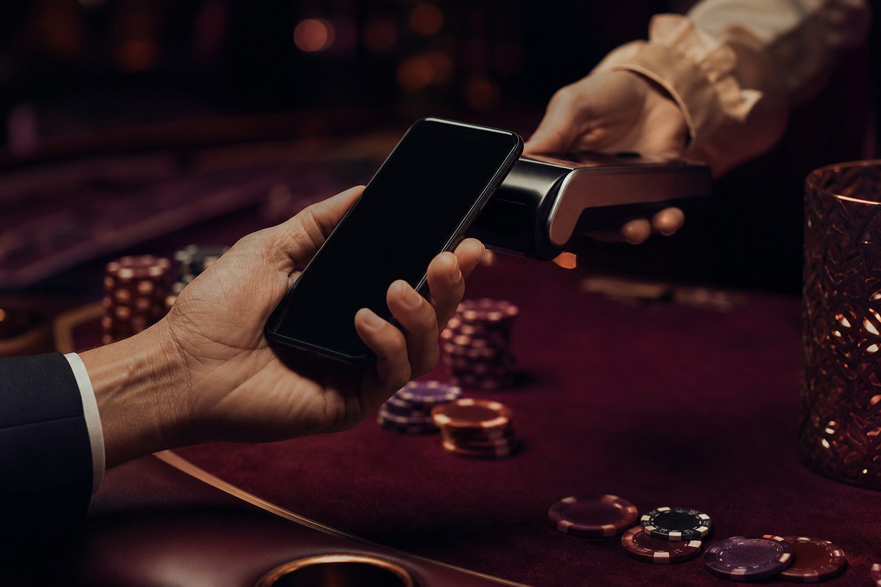Mano con un móvil sobre superficie granate con fichas de casino difuminadas